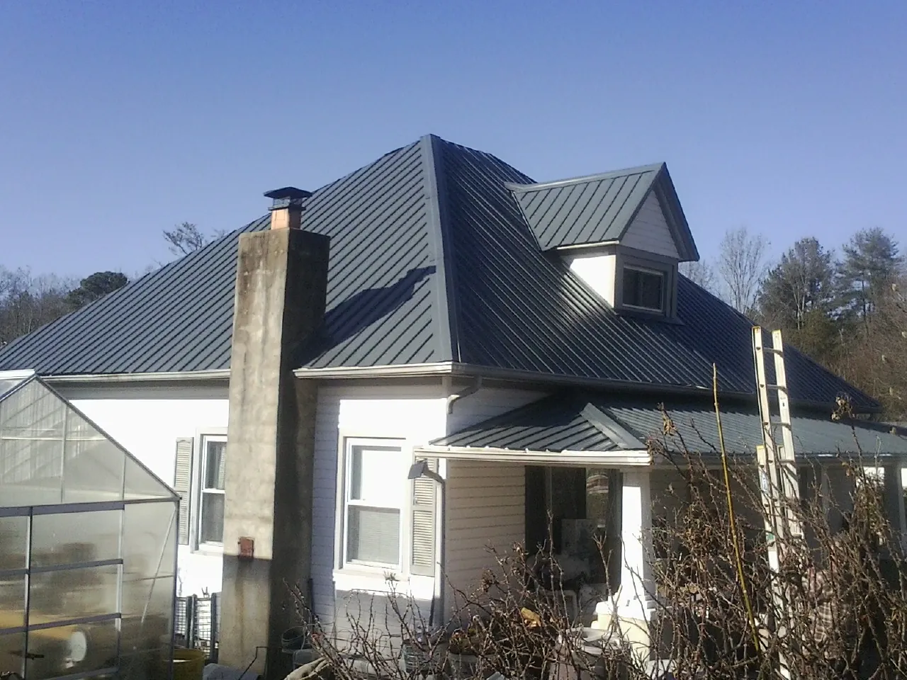 Dark blue standing seam metal roof on a white farmhouse with dormer — Slate & Tile Roof Repair by Roofing Brothers in Aquebogue