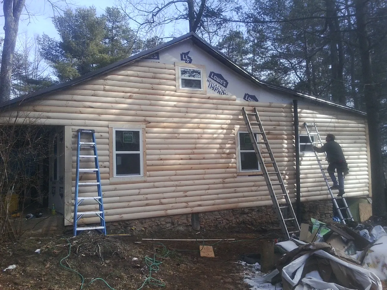 Ladders set against fresh log siding during an exterior remodel in Aquebogue
