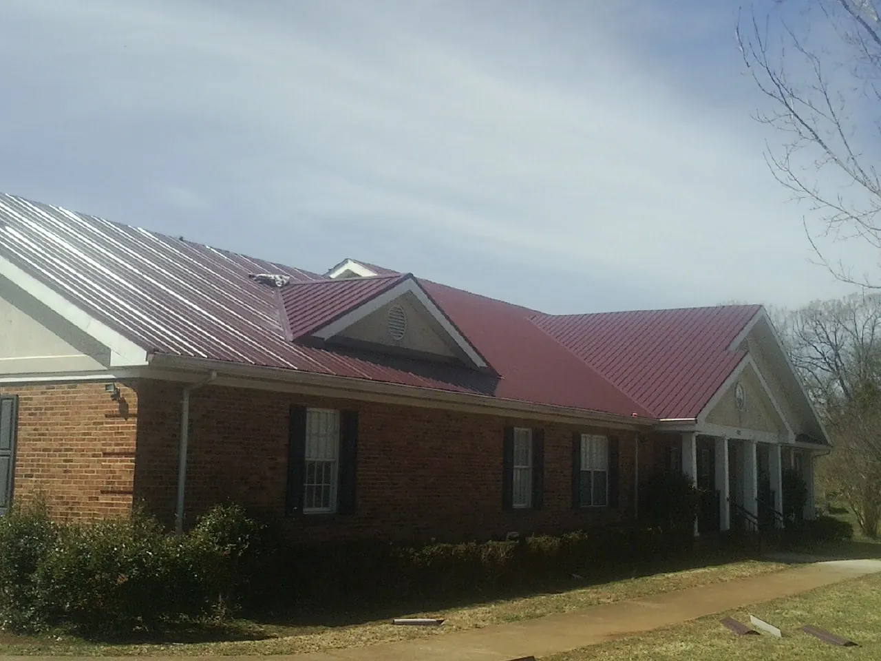 Red metal roof with gabled entries on a long brick building, from a Hail Damage Roof Repair job in Aquebogue