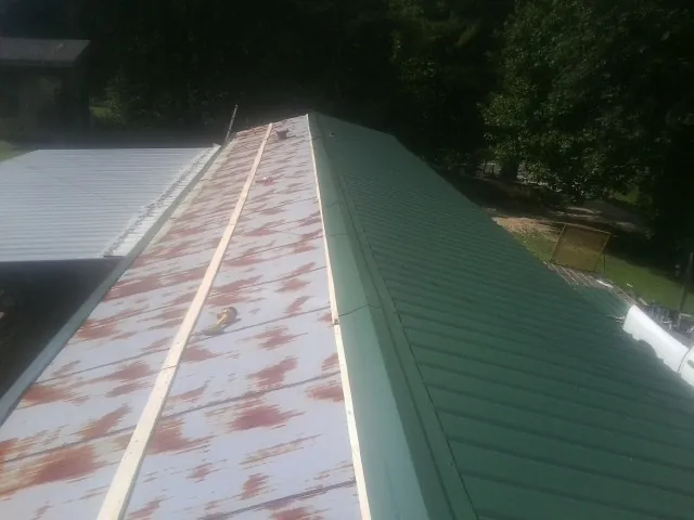 Old rusted panels beside newly installed green metal roofing — Wind Damage Roof Repair by Roofing Brothers in Aquebogue