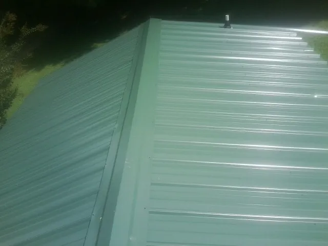 New green metal panels meeting at the ridge of a roof — Flat Roof Repair work by our crew in Aquebogue