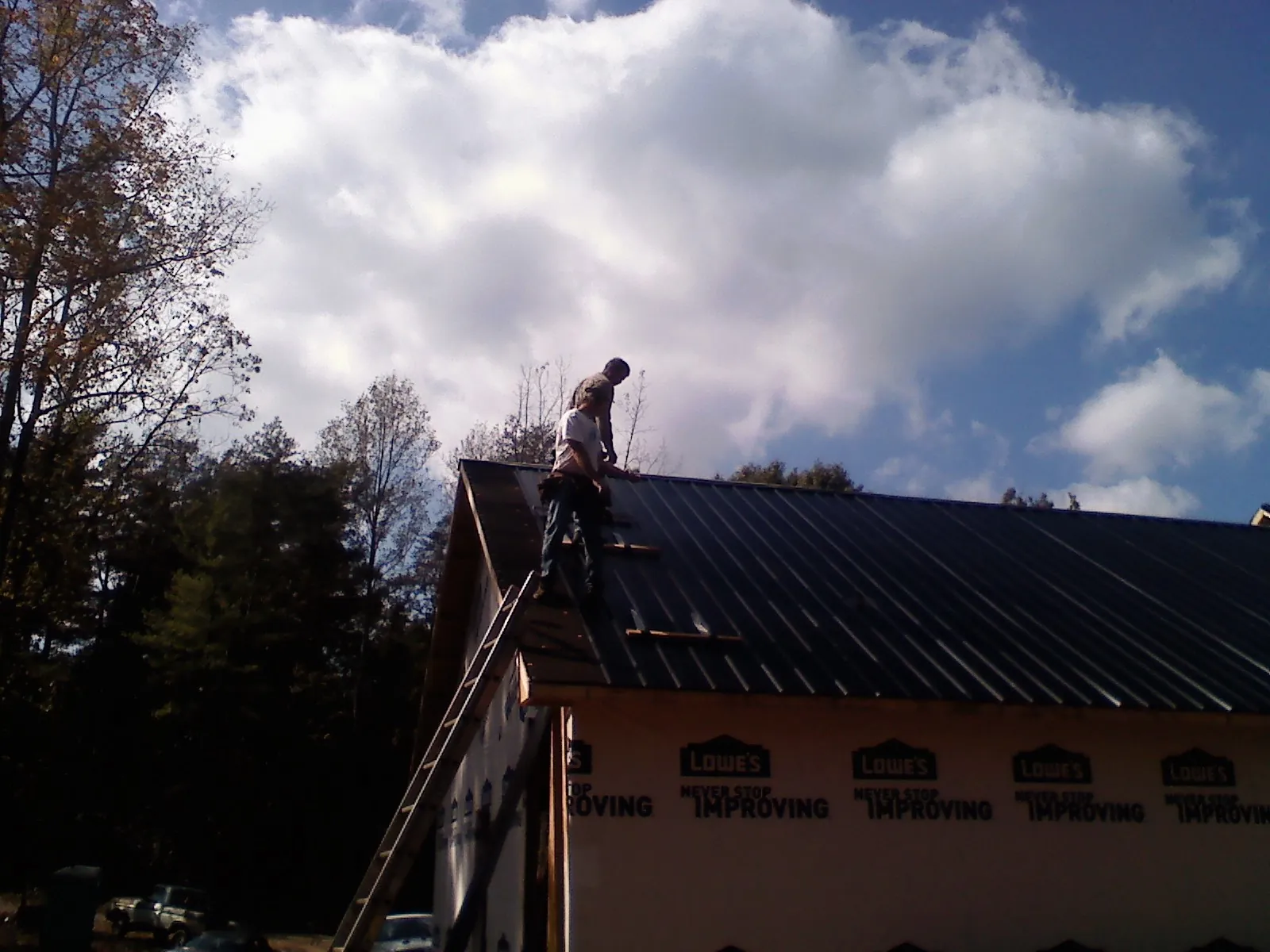Roofer fastening dark metal panels high against a cloudy sky, from a Roof Inspection job in Aquebogue