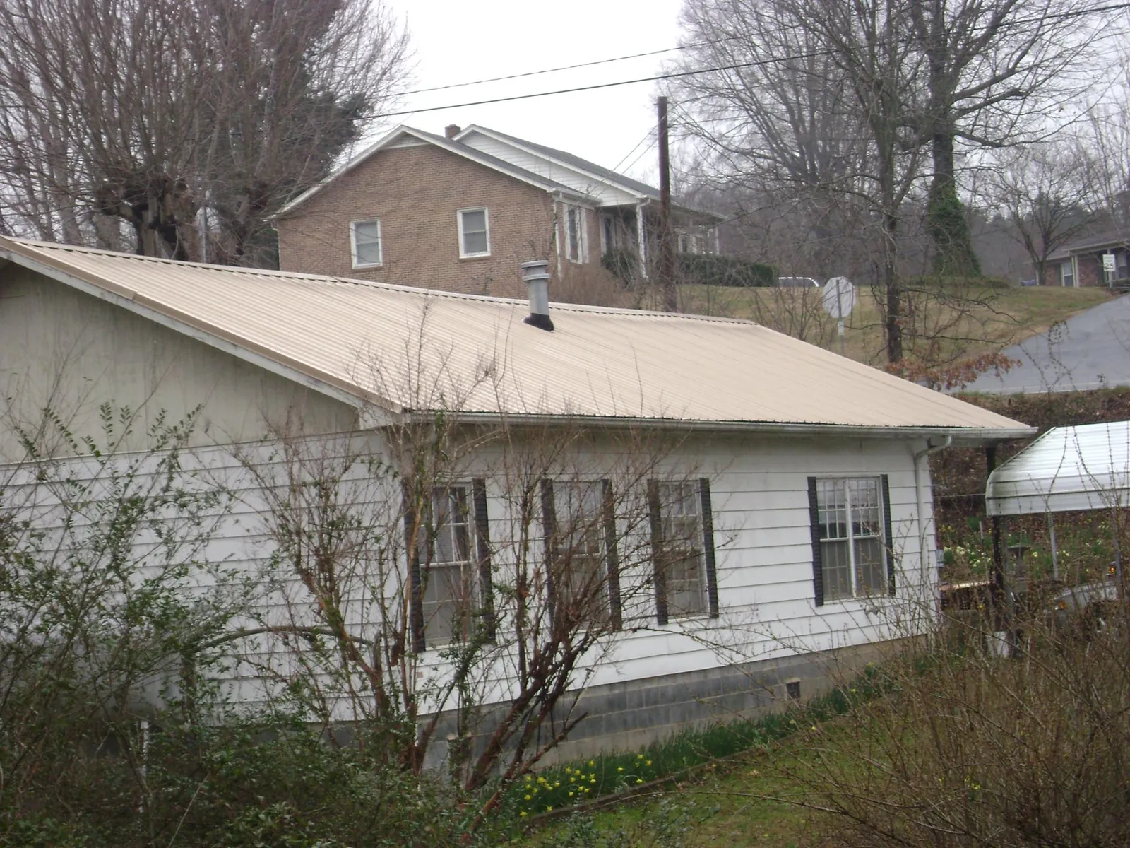 Tan metal roof on a white sided house set into a hillside — Commercial Roofing by Roofing Brothers in Aquebogue