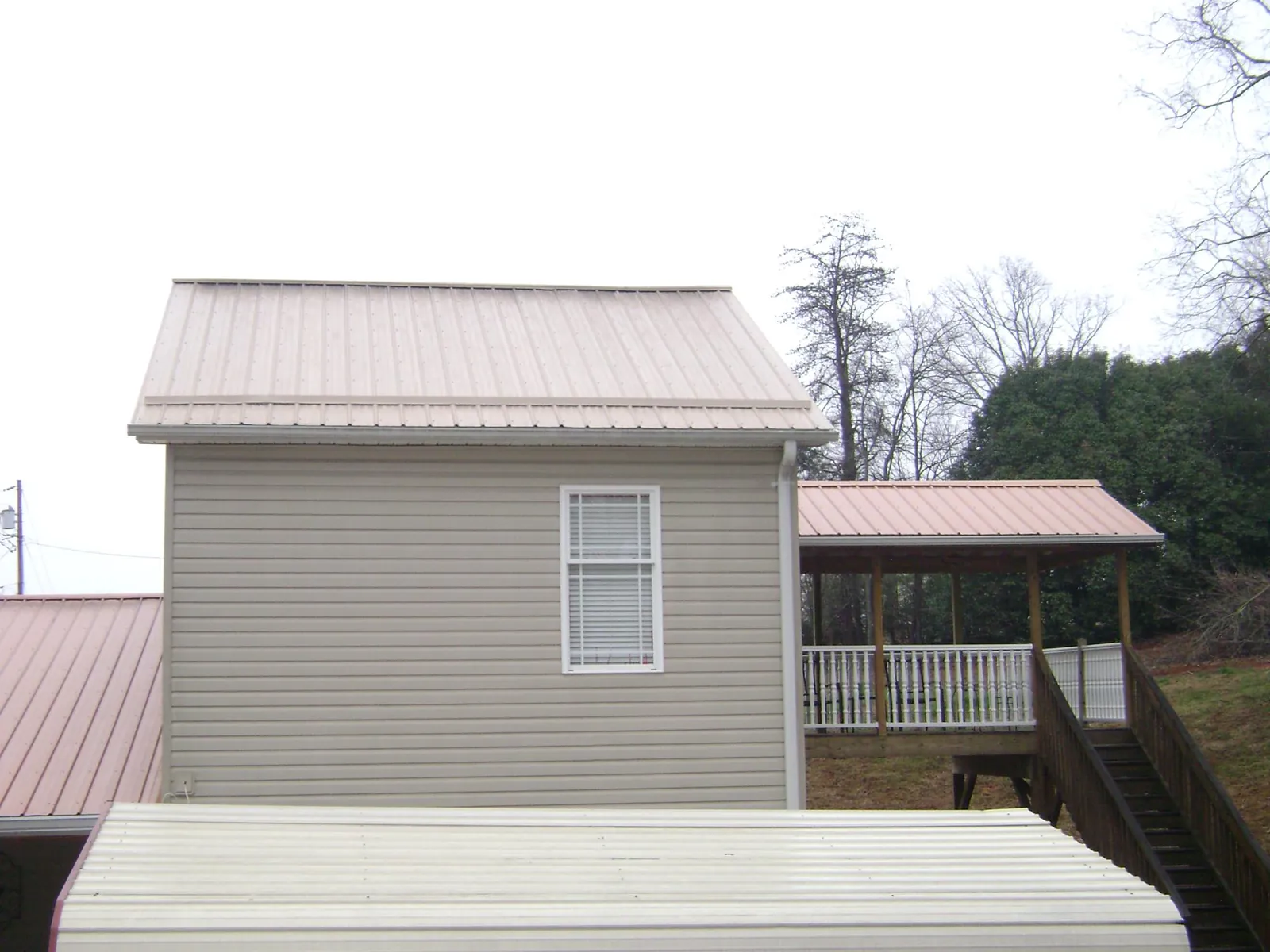 Tan metal roofs on a two story addition and attached porch, from a Roof Replacement job in Aquebogue